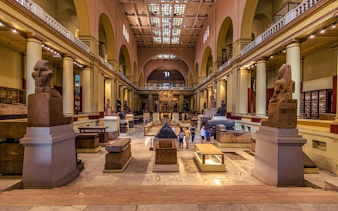 Grand Egyptian Museum interior with ancient statues and visitors exploring exhibits.