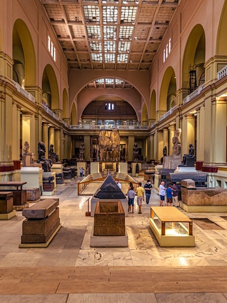 Grand Egyptian Museum interior with ancient statues and visitors exploring exhibits.