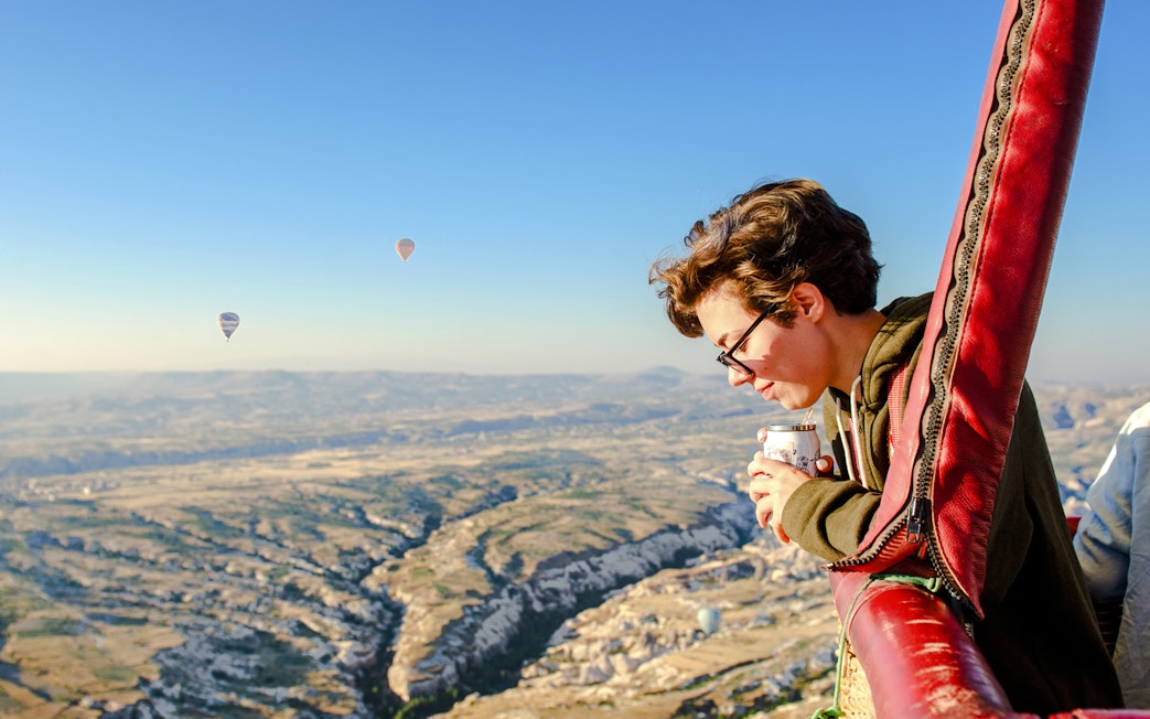 Person enjoying the view from a hot air balloon over Cappadocia landscape.