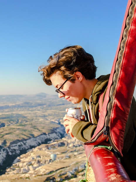 Person enjoying the view from a hot air balloon over Cappadocia landscape.