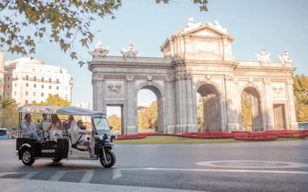 Tourists on an electric tuk-tuk passing Alcalá Gate in Madrid.