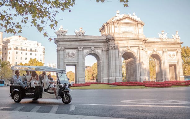 Tourists on an electric tuk-tuk passing Alcalá Gate in Madrid.
