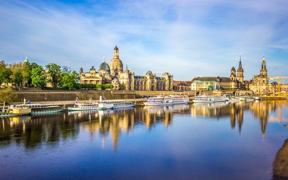 Elbe River cruise boats with Dresden skyline, including the Semperoper, reflected in the water.