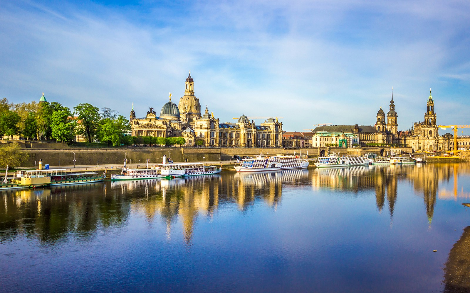 Elbe River cruise boats with Dresden skyline, including the Semperoper, reflected in the water.