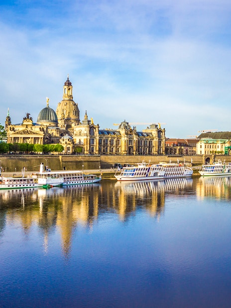 Elbe River cruise boats with Dresden skyline, including the Semperoper, reflected in the water.