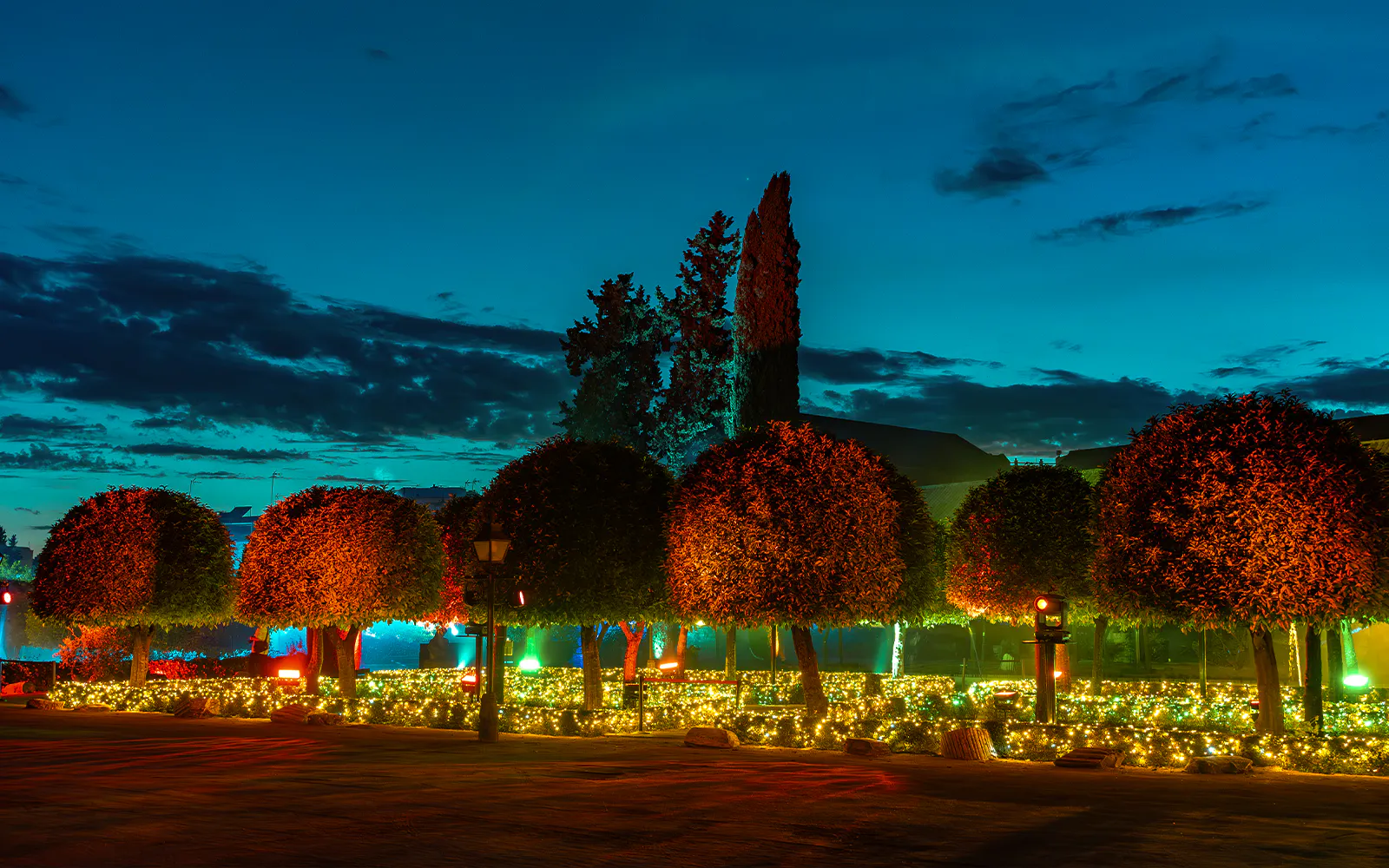 Alcazar of Cordoba garden illuminated at night with trees and decorative lights.