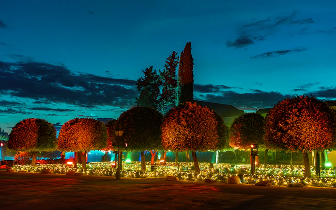 Alcazar of Cordoba garden illuminated at night with trees and decorative lights.