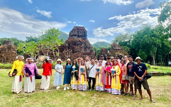 Group of tourists at My Son Sanctuary, Vietnam, with ancient temple ruins in the background.