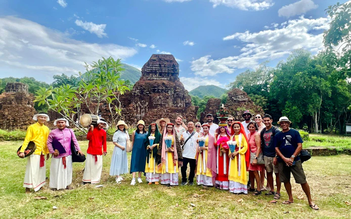 Group of tourists at My Son Sanctuary, Vietnam, with ancient temple ruins in the background.