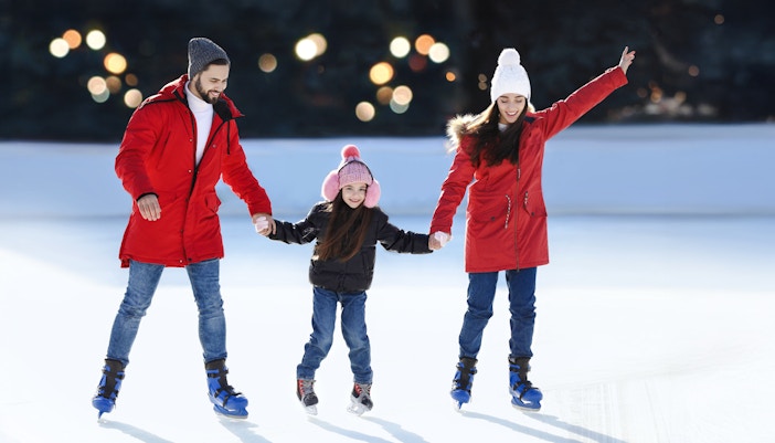Family ice skating together at an outdoor rink.