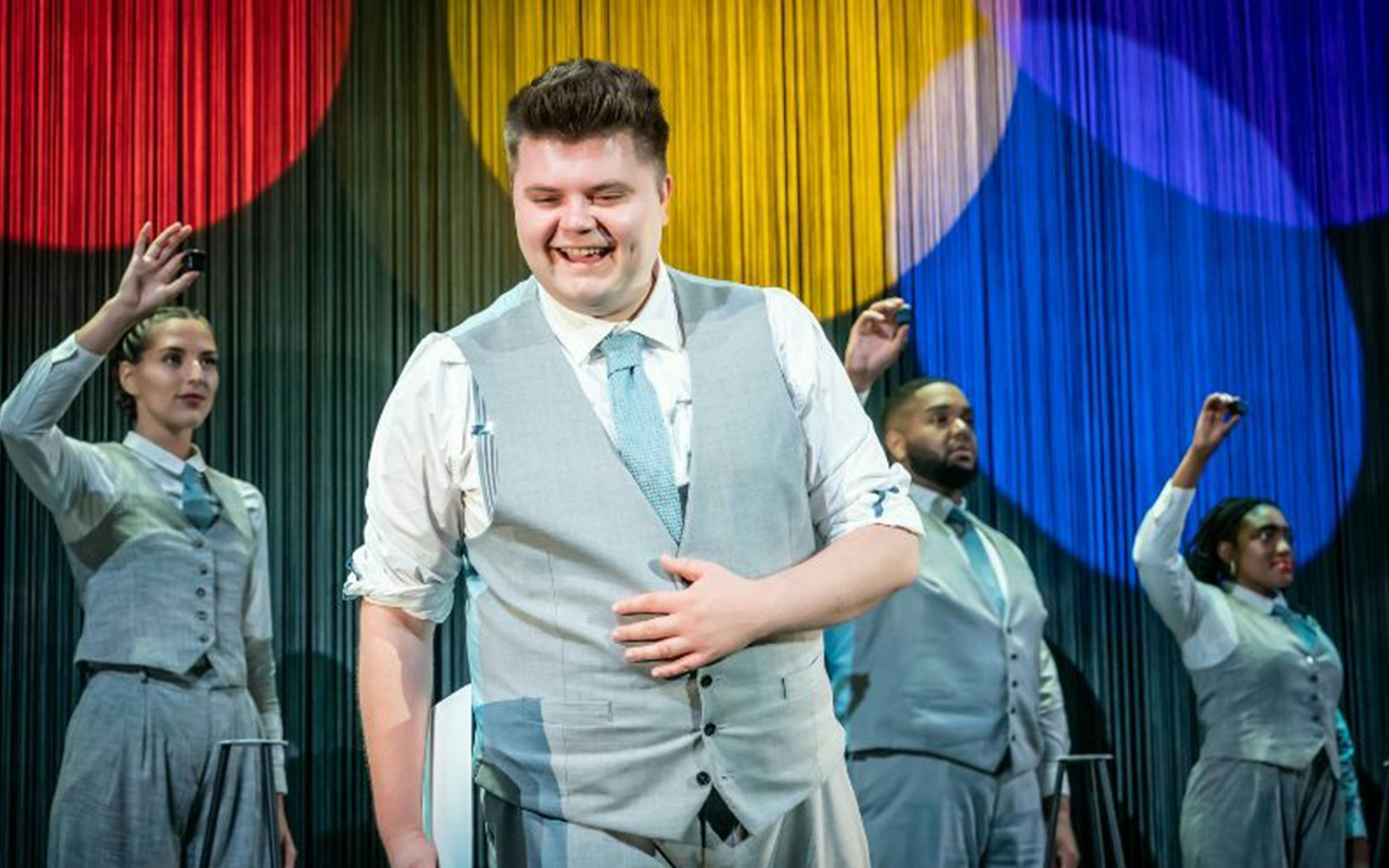 Performers in gray suits on stage with colorful backdrop during "Unbelievable" show.