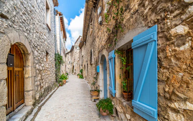 Narrow cobblestone street in a Provence village with stone houses and blue shutters.
