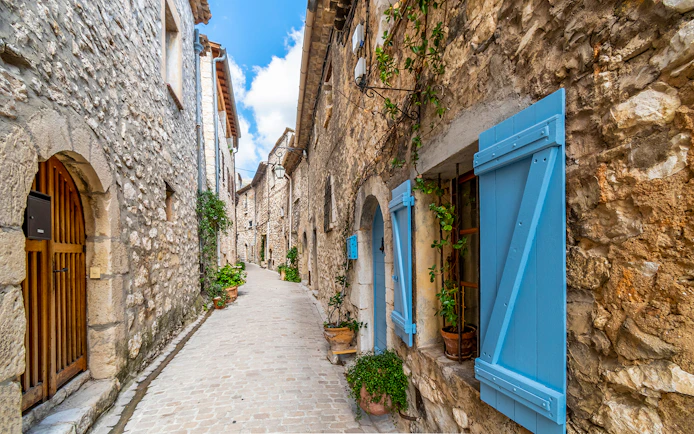 Narrow cobblestone street in a Provence village with stone houses and blue shutters.