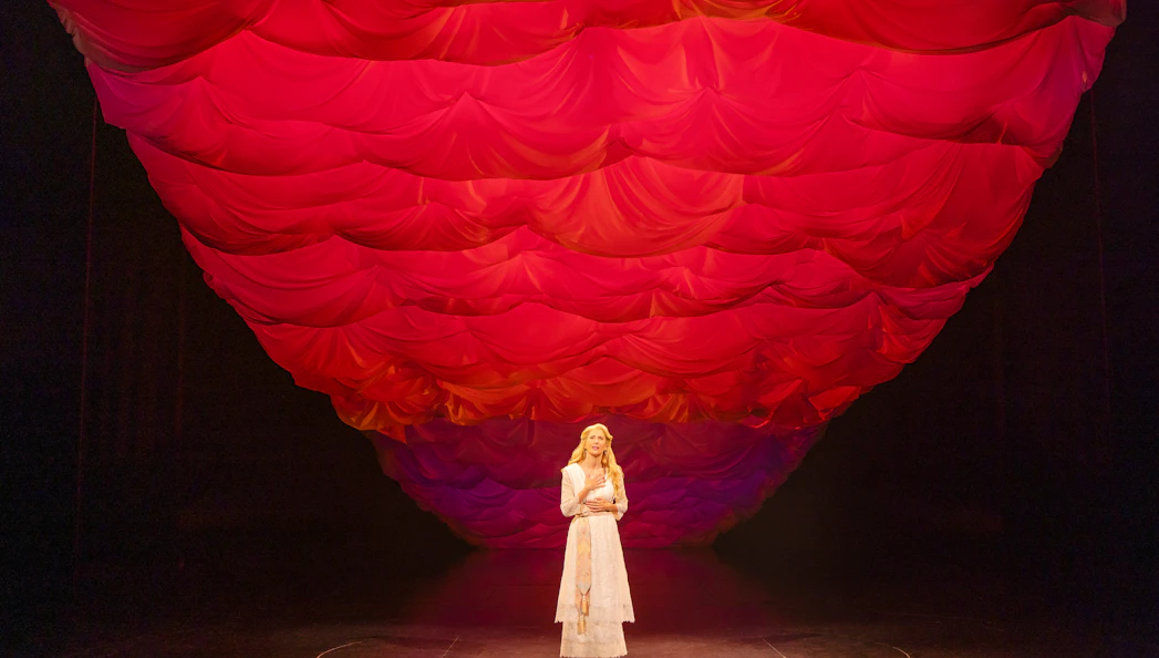 Performer on stage under red draped backdrop in Ragtime musical scene.