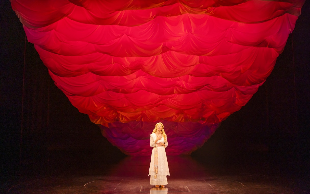 Performer on stage under red draped backdrop in Ragtime musical scene.