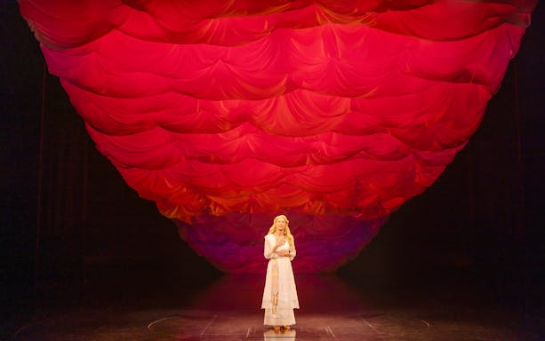 Performer on stage under red draped backdrop in Ragtime musical scene.