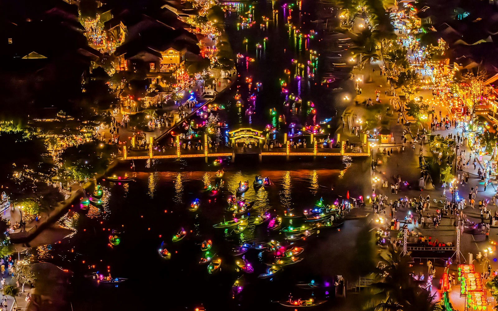 Hoi An river at night with colorful lanterns and boats, bustling with people.