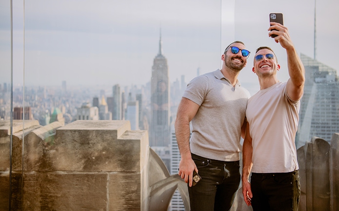 Two people taking a selfie at Top of the Rock Observation Deck with New York City skyline.