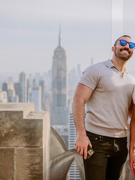 Two people taking a selfie at Top of the Rock Observation Deck with New York City skyline.