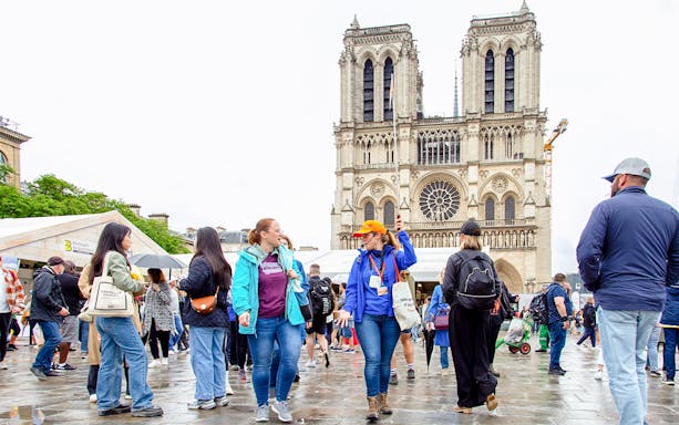 Tourists outside Notre Dame de Paris, viewing facade and entering cathedral's crypt.