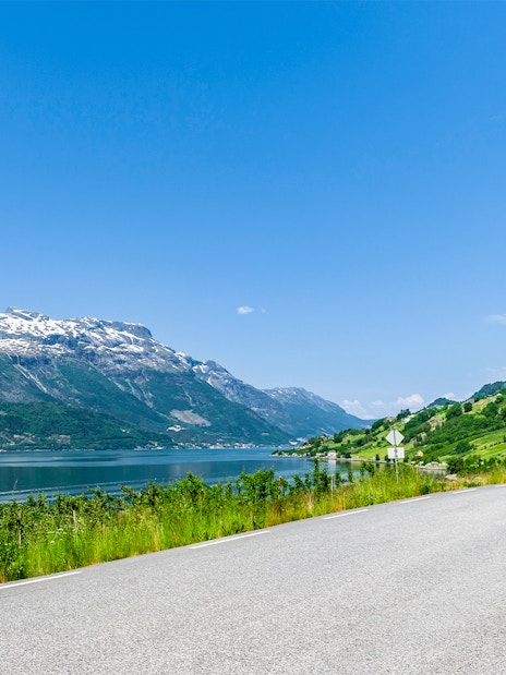 Scenic road along Hardangerfjord with mountains and clear blue sky.