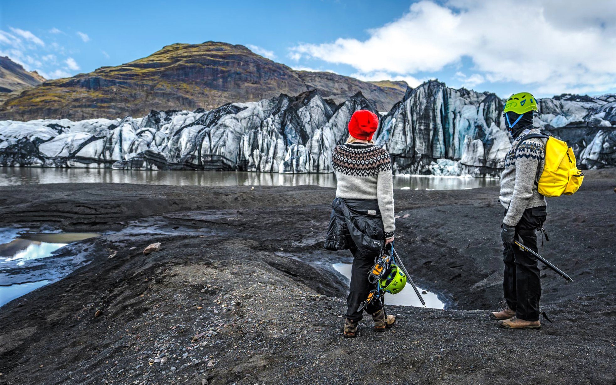 Tourists with gear at Reynisfjara black-sand beach, Iceland, viewing glacier.