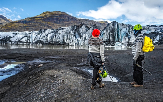 Tourists with gear at Reynisfjara black-sand beach, Iceland, viewing glacier.