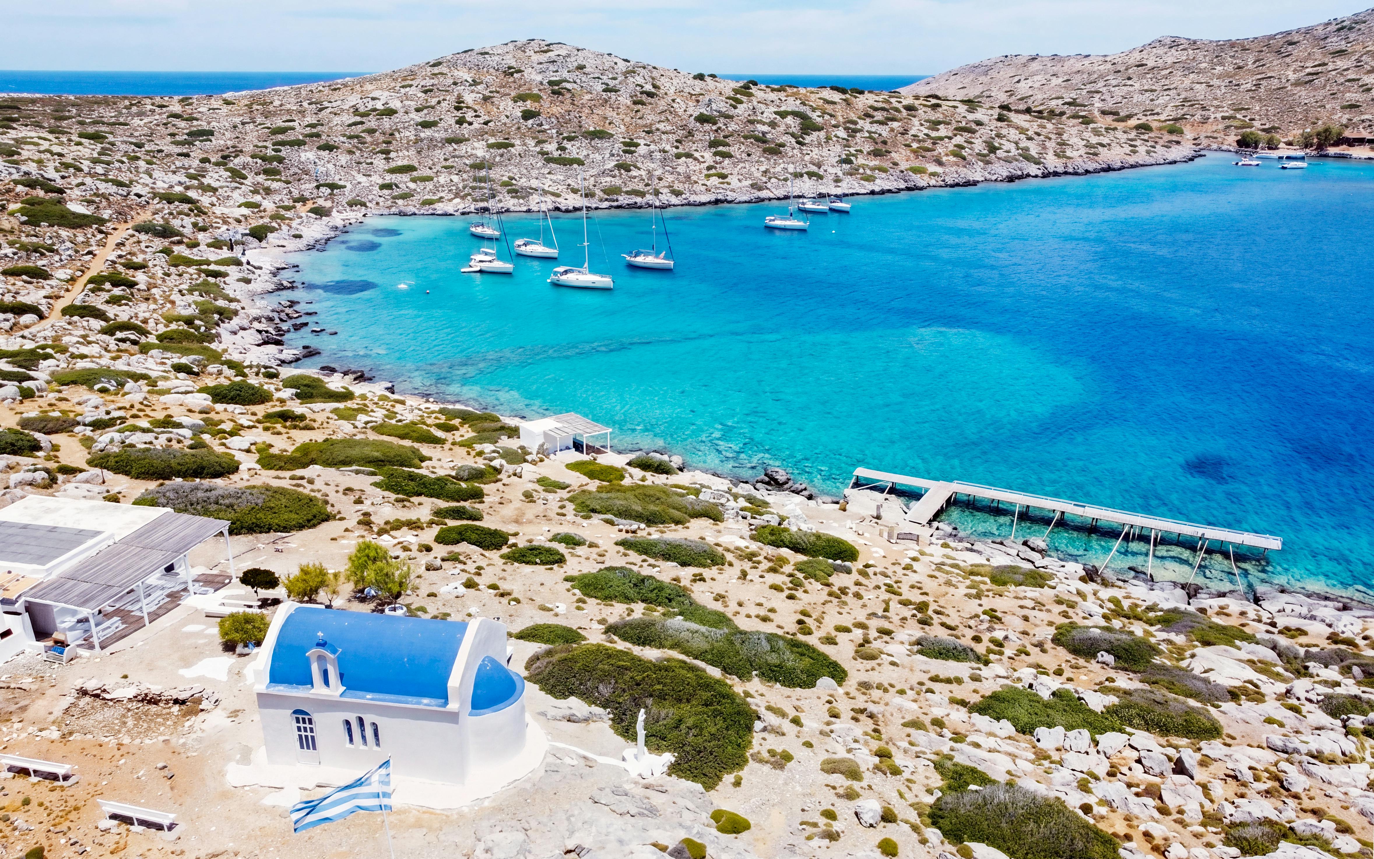 Heraklion catamaran cruise with yachts in turquoise bay near rocky coastline and white chapel.