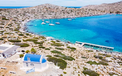 Heraklion catamaran cruise with yachts in turquoise bay near rocky coastline and white chapel.
