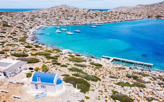 Heraklion catamaran cruise with yachts in turquoise bay near rocky coastline and white chapel.