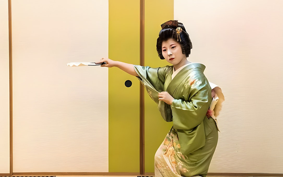 Geisha in green kimono performing traditional dance with fan in Japan.