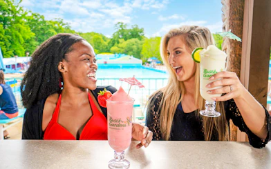 Visitors enjoying frozen drinks at Water Country USA, Williamsburg, with a pool in the background.