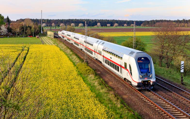 Intercity train traveling through rural Germany with fields and trees in the background.