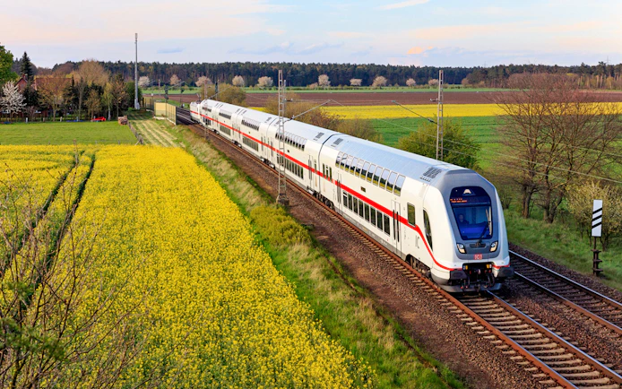 Intercity train traveling through rural Germany with fields and trees in the background.