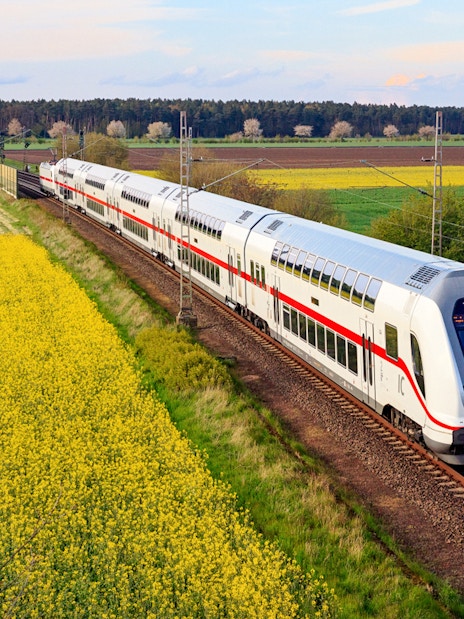 Intercity train traveling through rural Germany with fields and trees in the background.