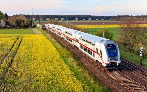 Intercity train traveling through rural Germany with fields and trees in the background.