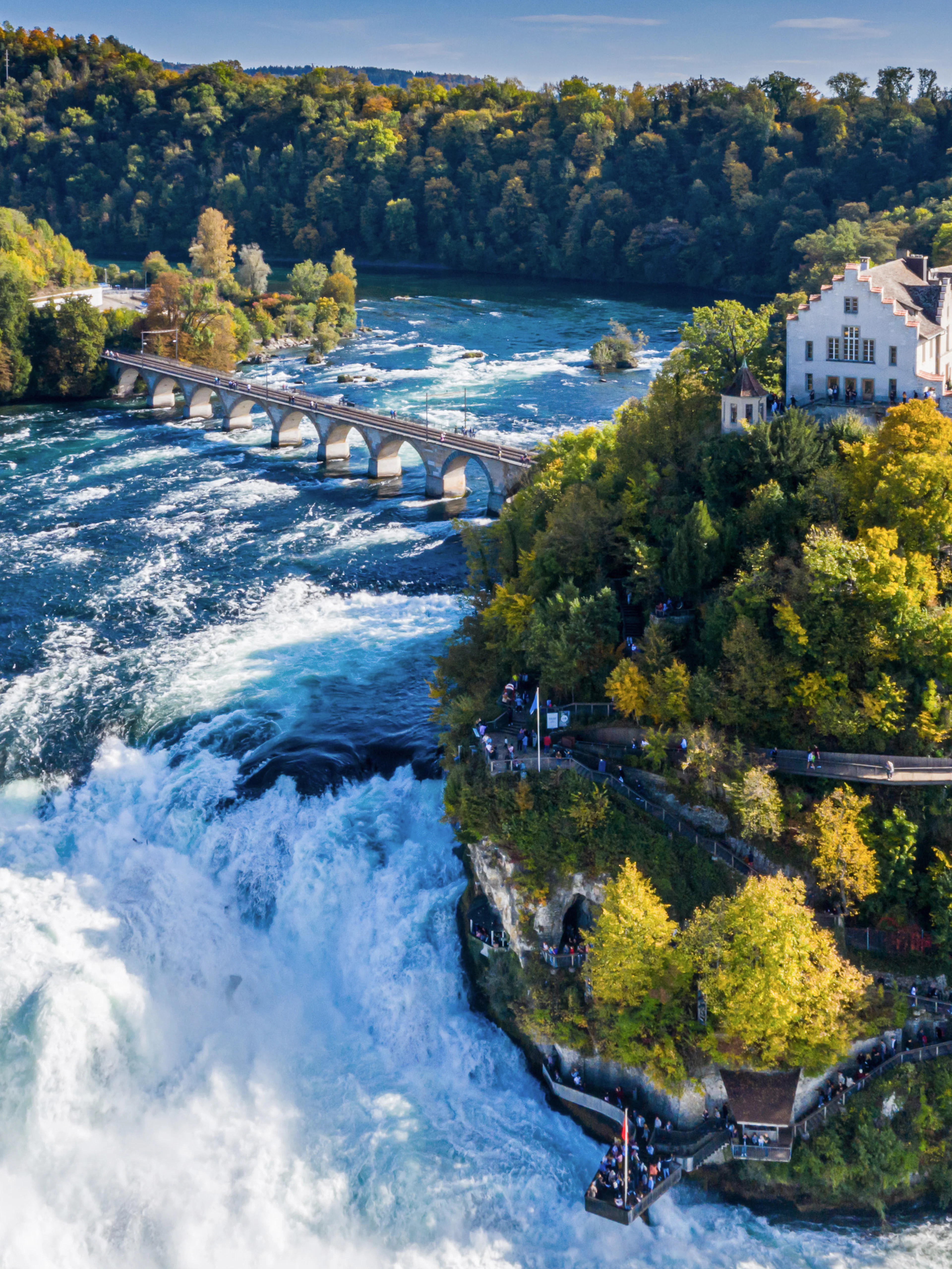Panoramic aerial view of Rhine Falls, Switzerland, with surrounding lush greenery and historic buildings.