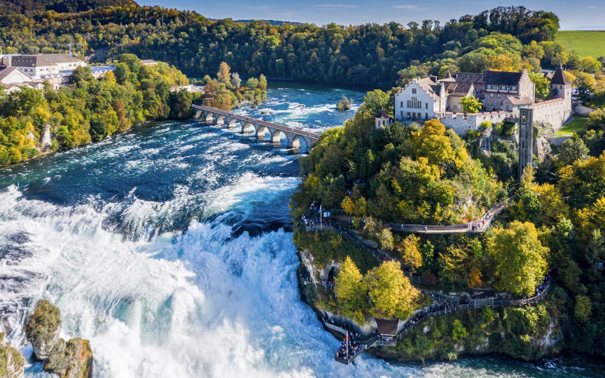 Panoramic aerial view of Rhine Falls, Switzerland, with surrounding lush greenery and historic buildings.