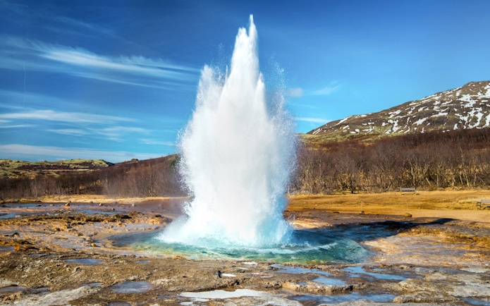Geyser erupting in the Golden Circle, Iceland with snowy hills in the background.
