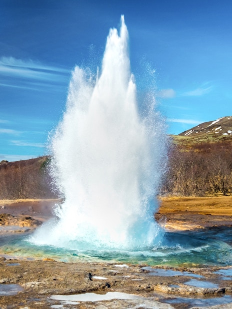 Geyser erupting in the Golden Circle, Iceland with snowy hills in the background.