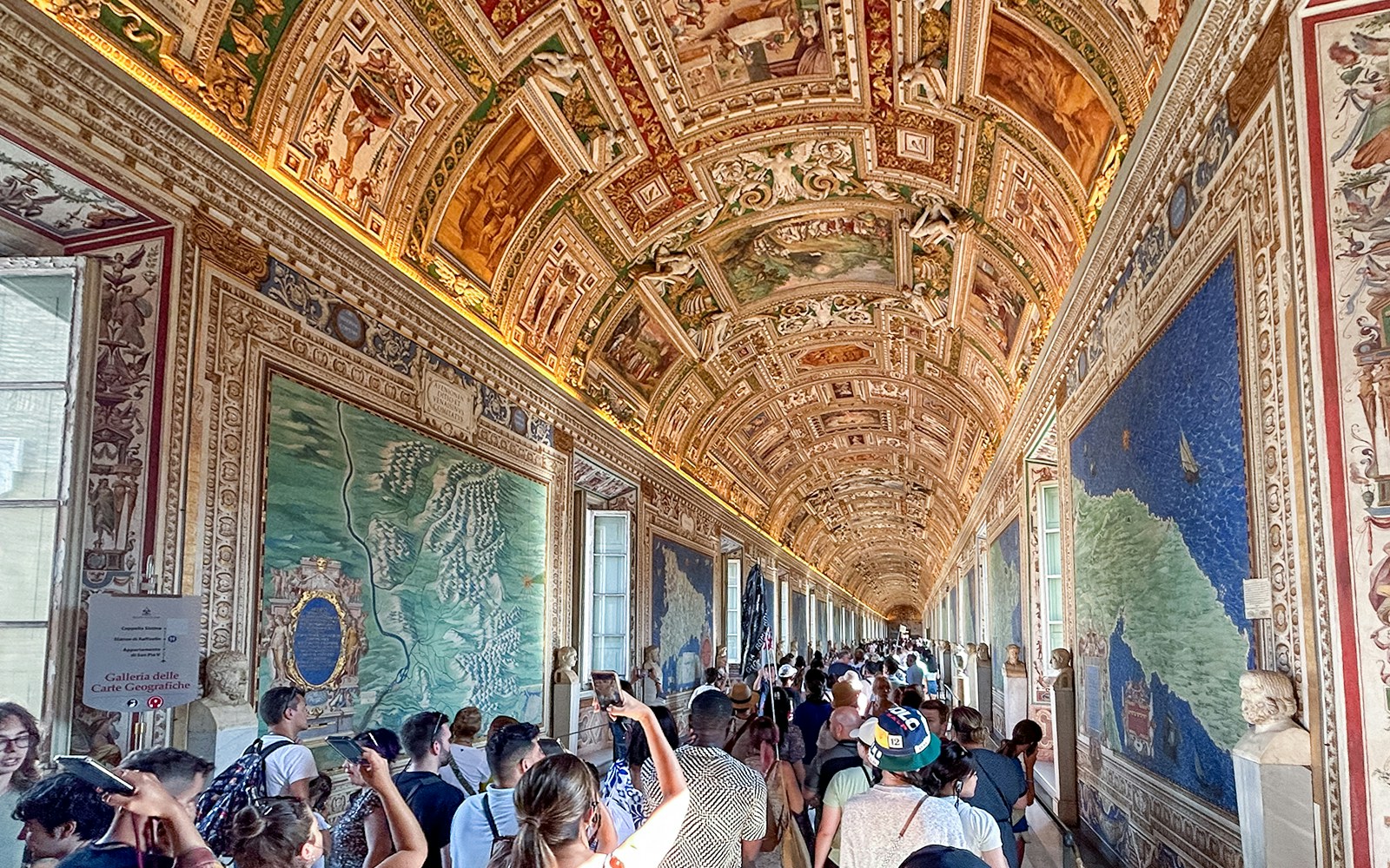 Visitors exploring the Gallery of Maps in the Vatican Museum, admiring detailed frescoes.