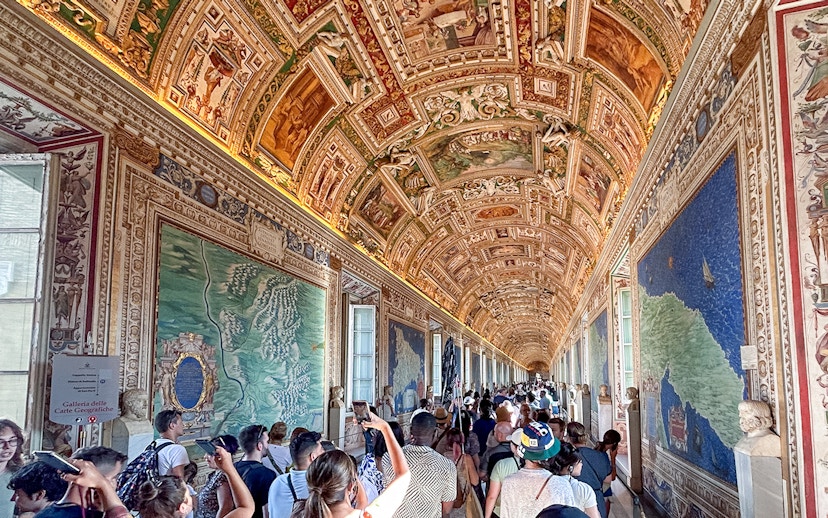 Visitors exploring the Gallery of Maps in the Vatican Museum, admiring detailed frescoes.