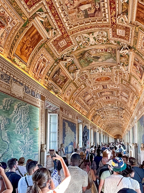 Visitors exploring the Gallery of Maps in the Vatican Museum, admiring detailed frescoes.