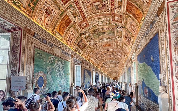 Visitors exploring the Gallery of Maps in the Vatican Museum, admiring detailed frescoes.