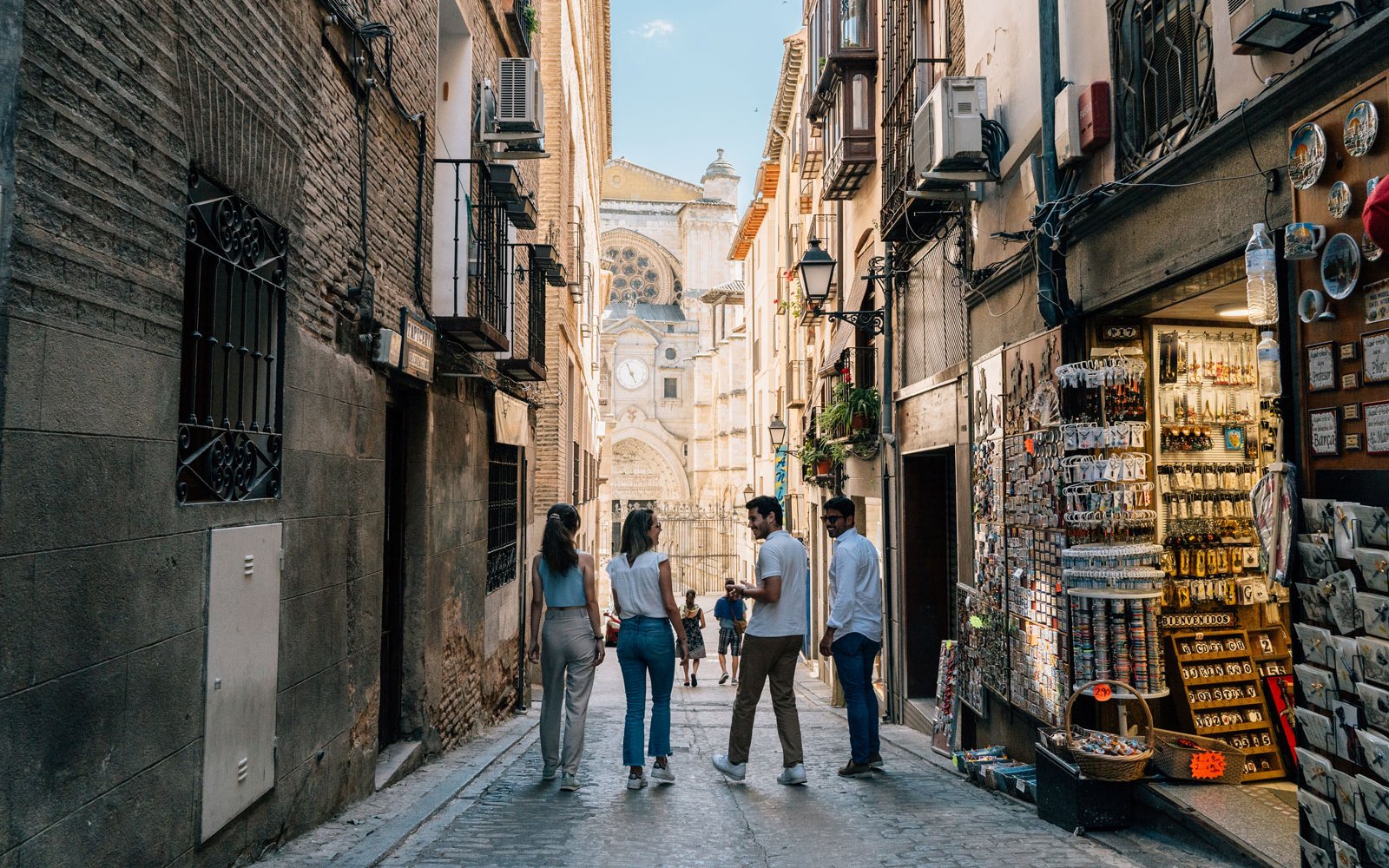 People walking through a narrow street in Toledo, Spain, with Toledo Cathedral in the background.