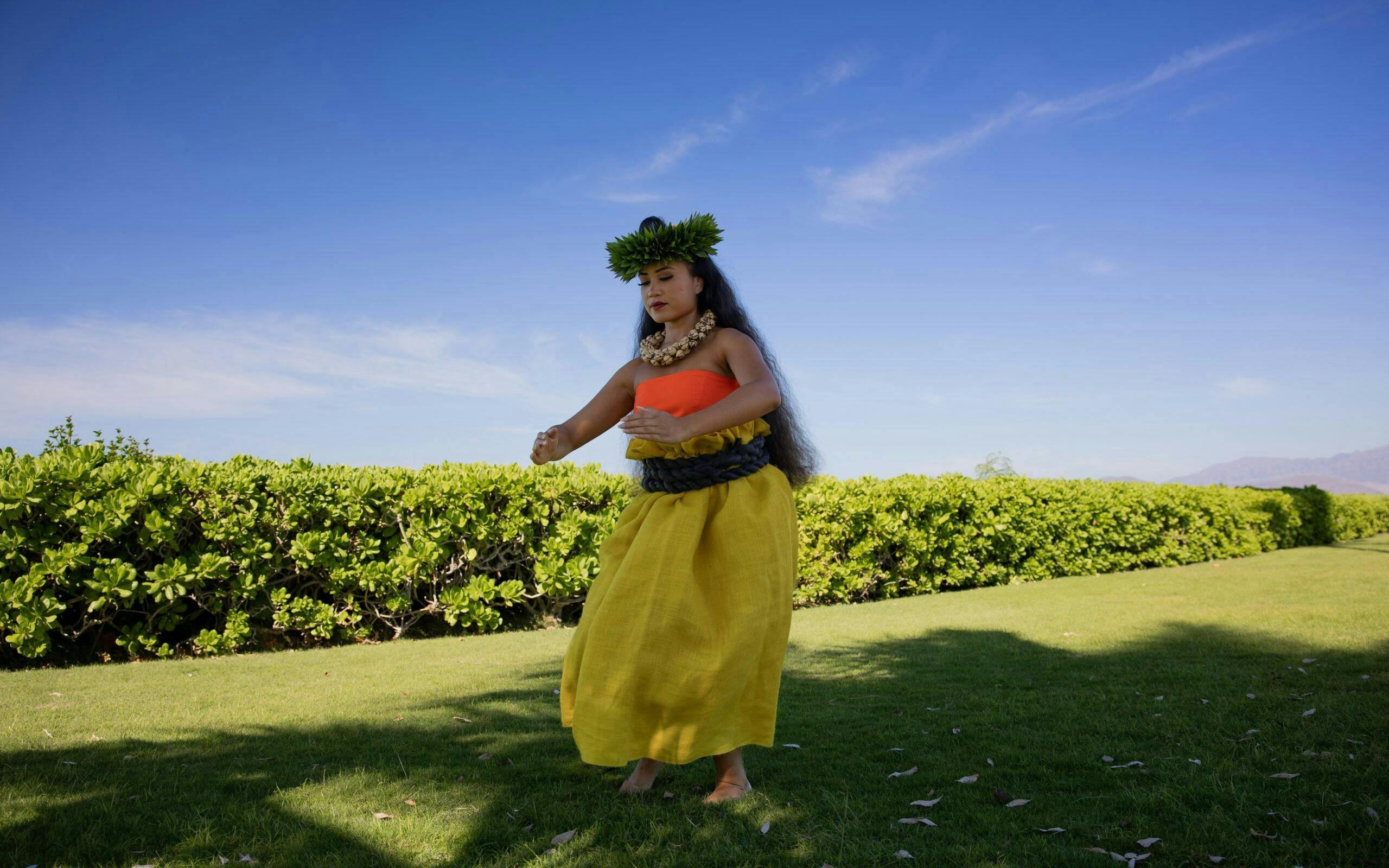 Hula dancer performing at Kaula-Luau with greenery and blue sky backdrop.