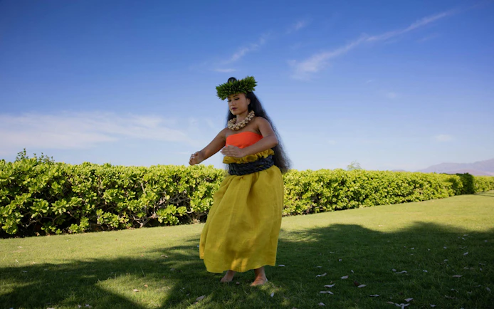 Hula dancer performing at Kaula-Luau with greenery and blue sky backdrop.