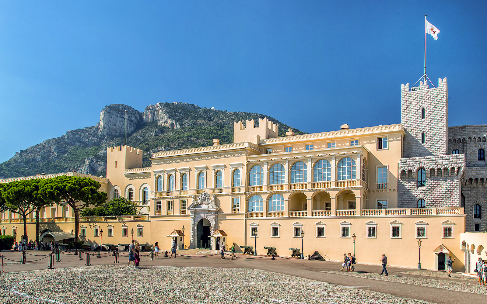 Tourists exploring the Prince's Palace of Monaco with mountain backdrop on a French Riviera tour.