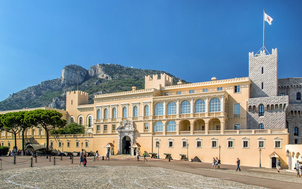 Tourists exploring the Prince's Palace of Monaco with mountain backdrop on a French Riviera tour.