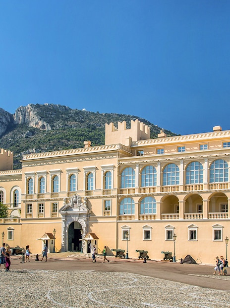 Tourists exploring the Prince's Palace of Monaco with mountain backdrop on a French Riviera tour.
